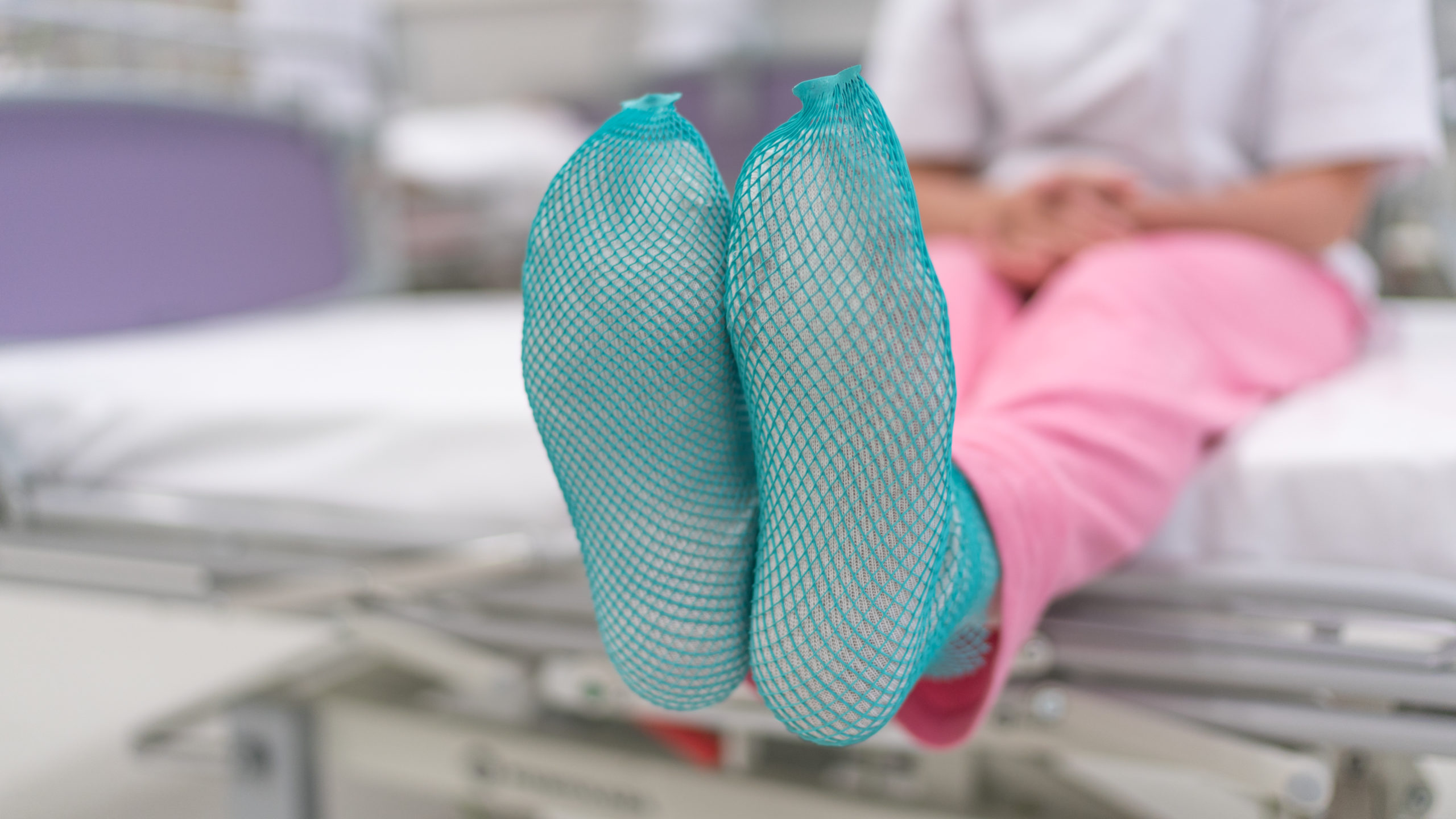 A person sits on a hospital bed wearing green mesh-like brake socks